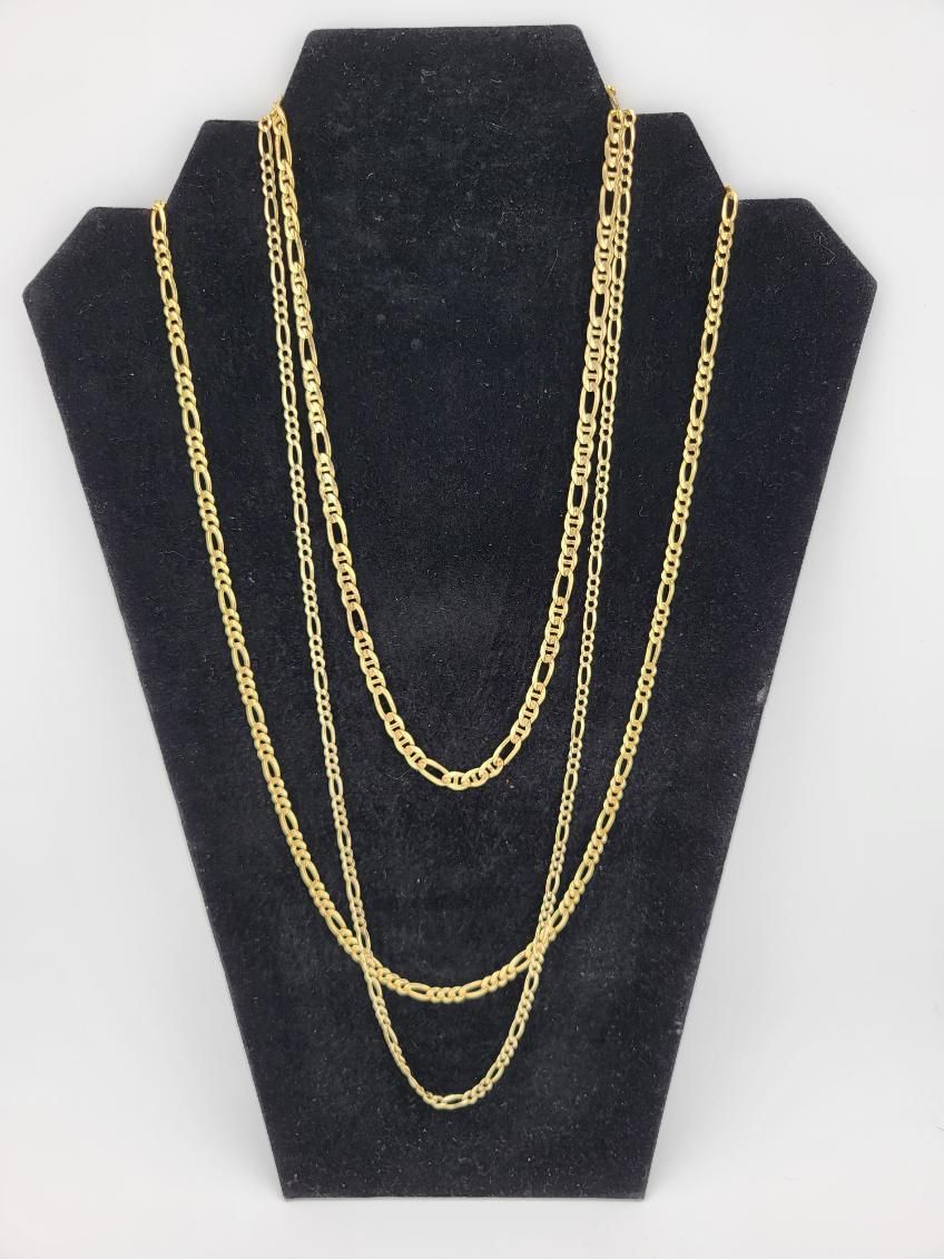 Three gold Figaro chain necklaces draped on a black jewelry display stand.