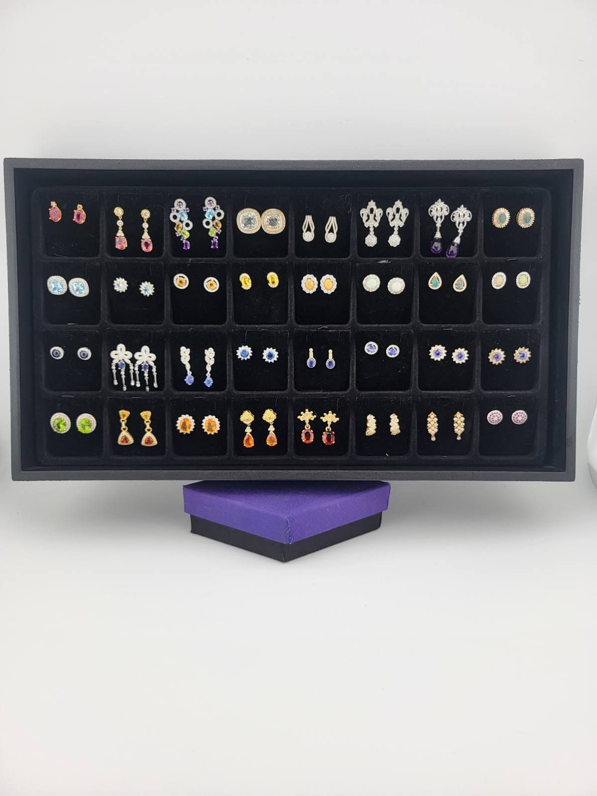 Black display tray of earrings on a purple box against a white background.