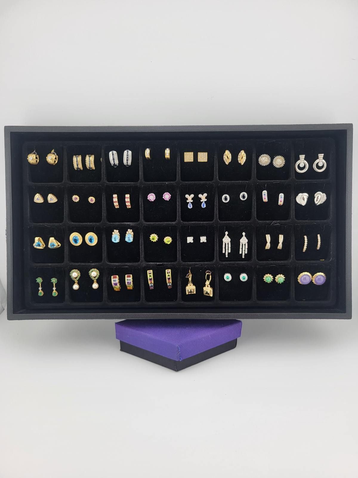 Black tray displaying various earrings; a purple jewelry box sits below.