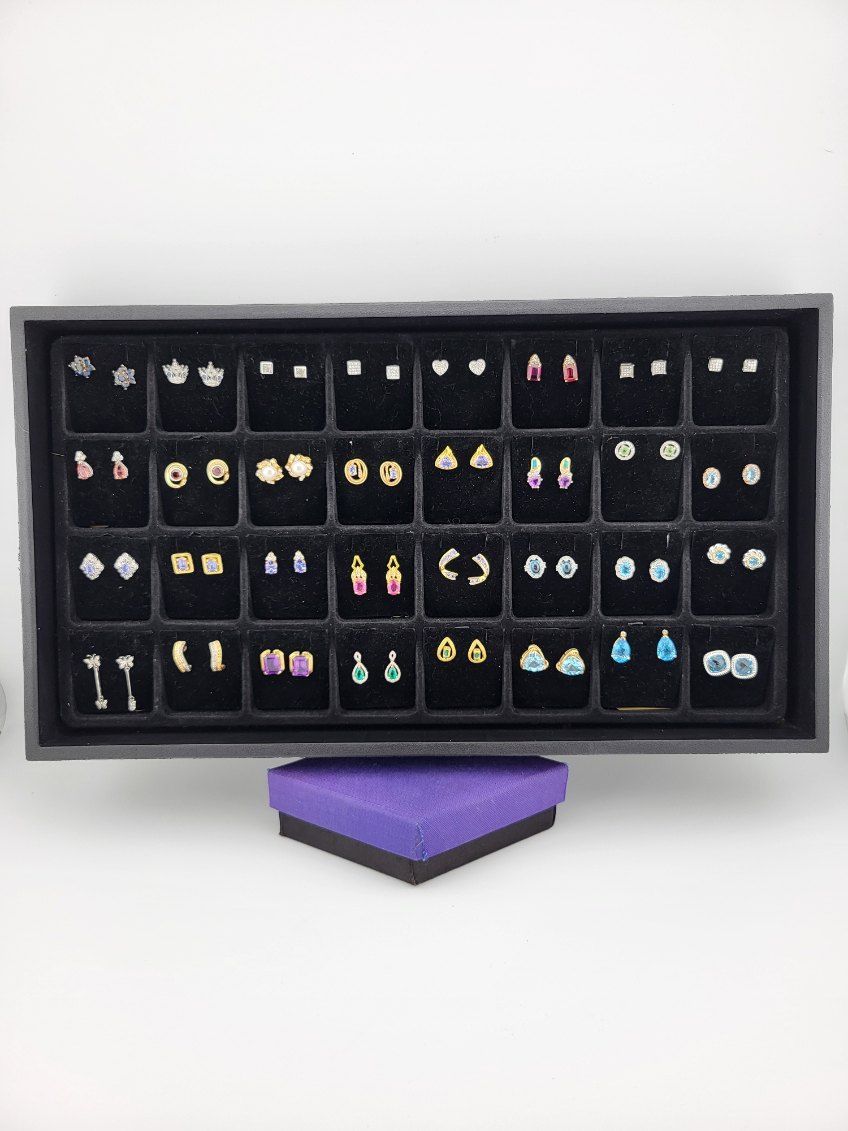 A tray of various stud earrings on a purple gift box, set on a white surface.