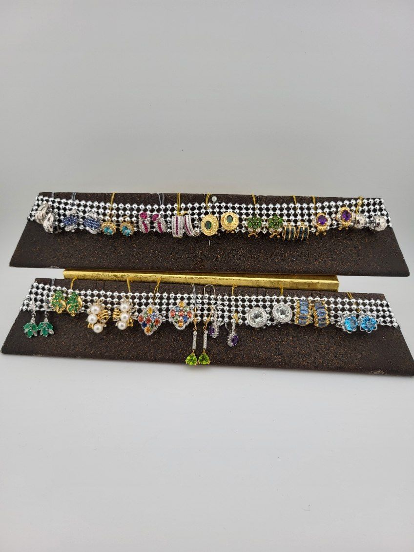 Two tiered display of various colorful gemstone earrings on a white backdrop.