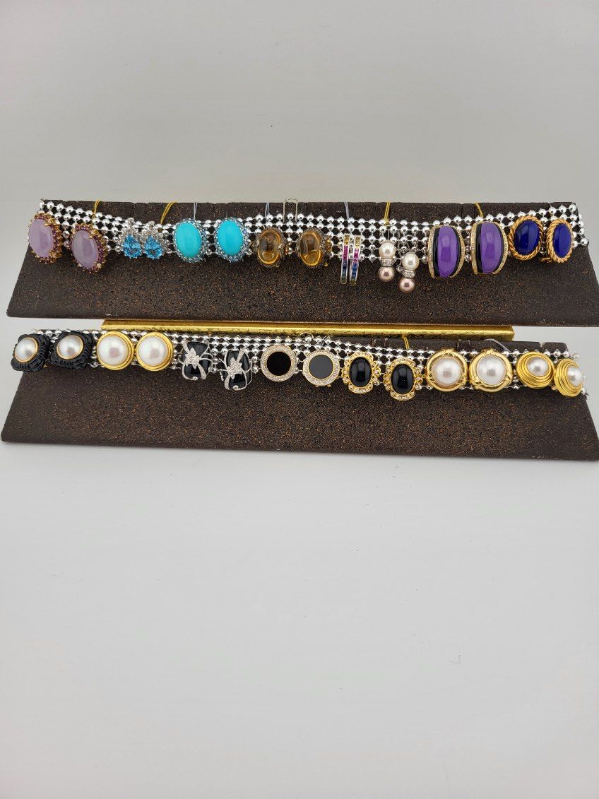Earrings displayed on a two-tiered brown tray with gemstones, pearls, and various metal settings.