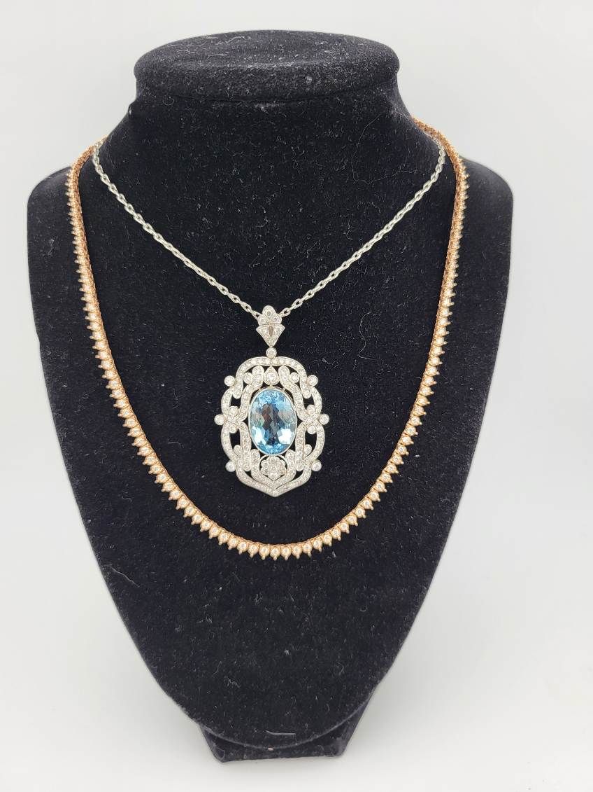 Two necklaces on a black jewelry display. One has a blue gem pendant, the other is gold-toned.