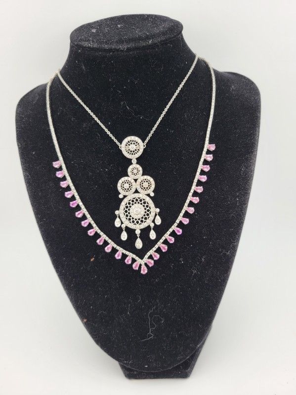 Two silver necklaces with gemstones displayed on a black jewelry bust.