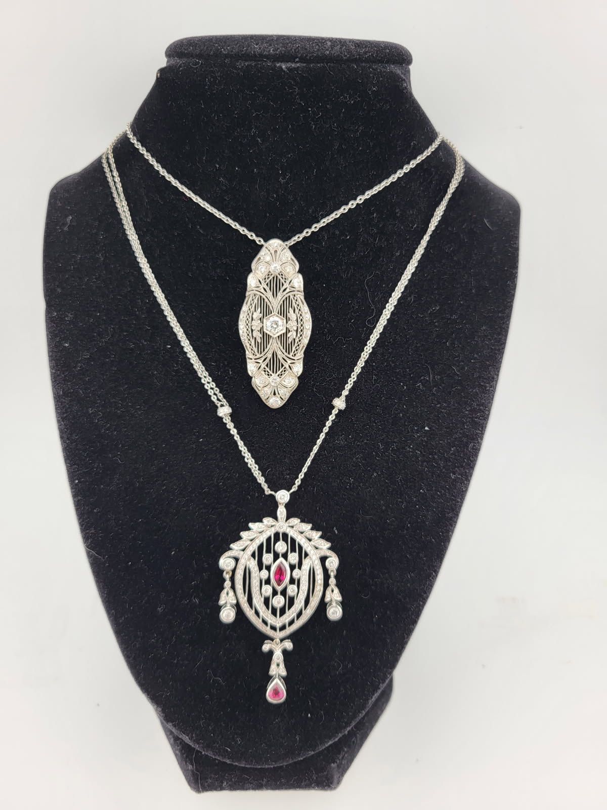 Two ornate silver necklaces with pendants displayed on a black jewelry stand.