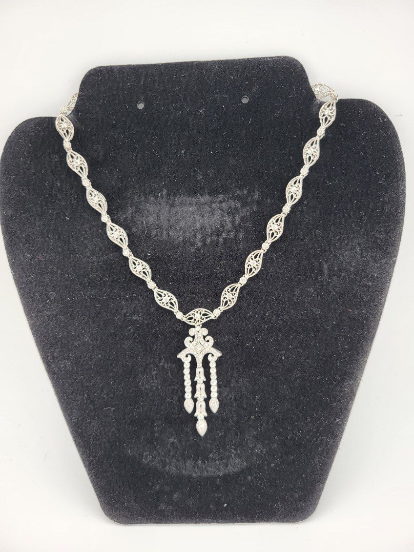 Silver filigree necklace on a black velvet bust.