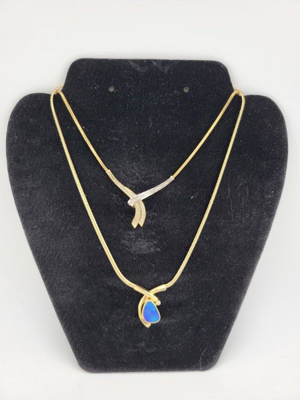 Two gold necklaces displayed on a black velvet bust. One has a blue gemstone pendant, the other a diamond cluster.