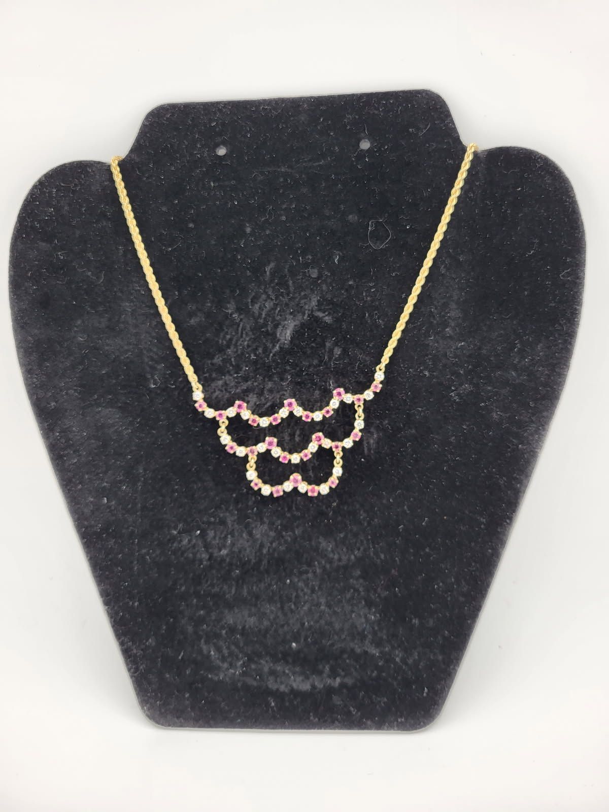 Gold necklace with a scalloped pendant, set with pink gemstones, on a black jewelry display.