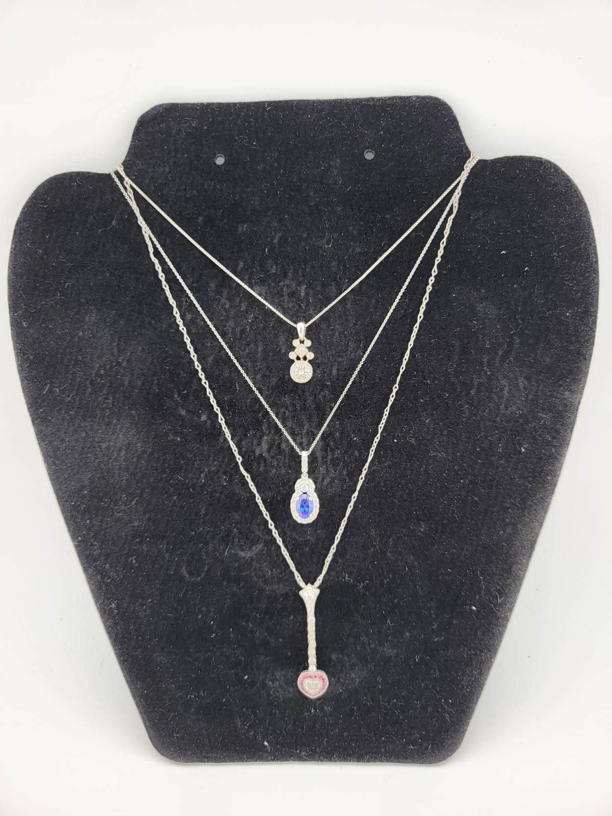 Three silver necklaces with gemstone pendants on a black velvet display stand.