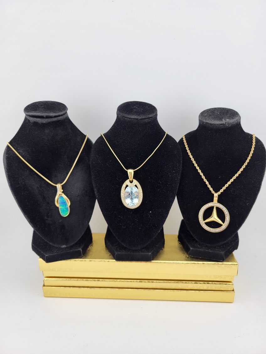 Three gold necklaces on black velvet busts, each with a different pendant.