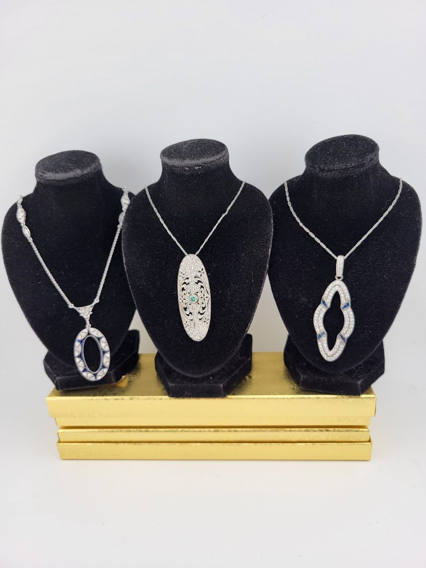 Three silver necklaces on black velvet stands, displayed on a gold rectangular base.