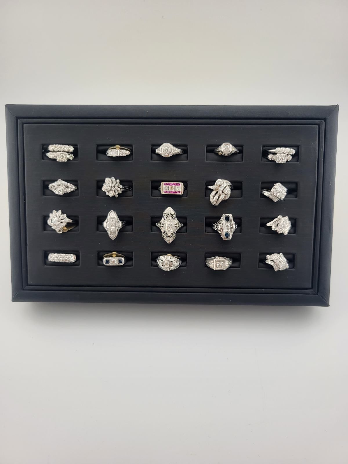 Black jewelry display case filled with engagement rings, set on a white surface.