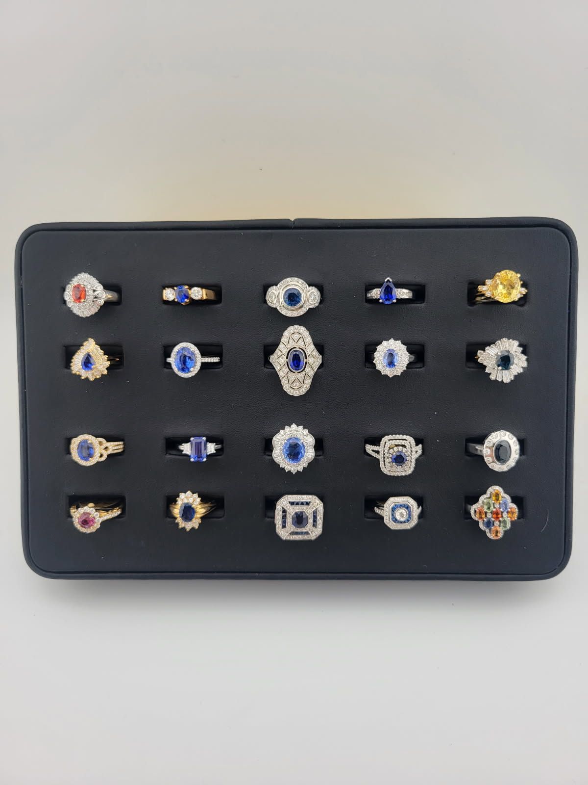 A display of 24 rings with various blue and white gemstones set in black jewelry display.