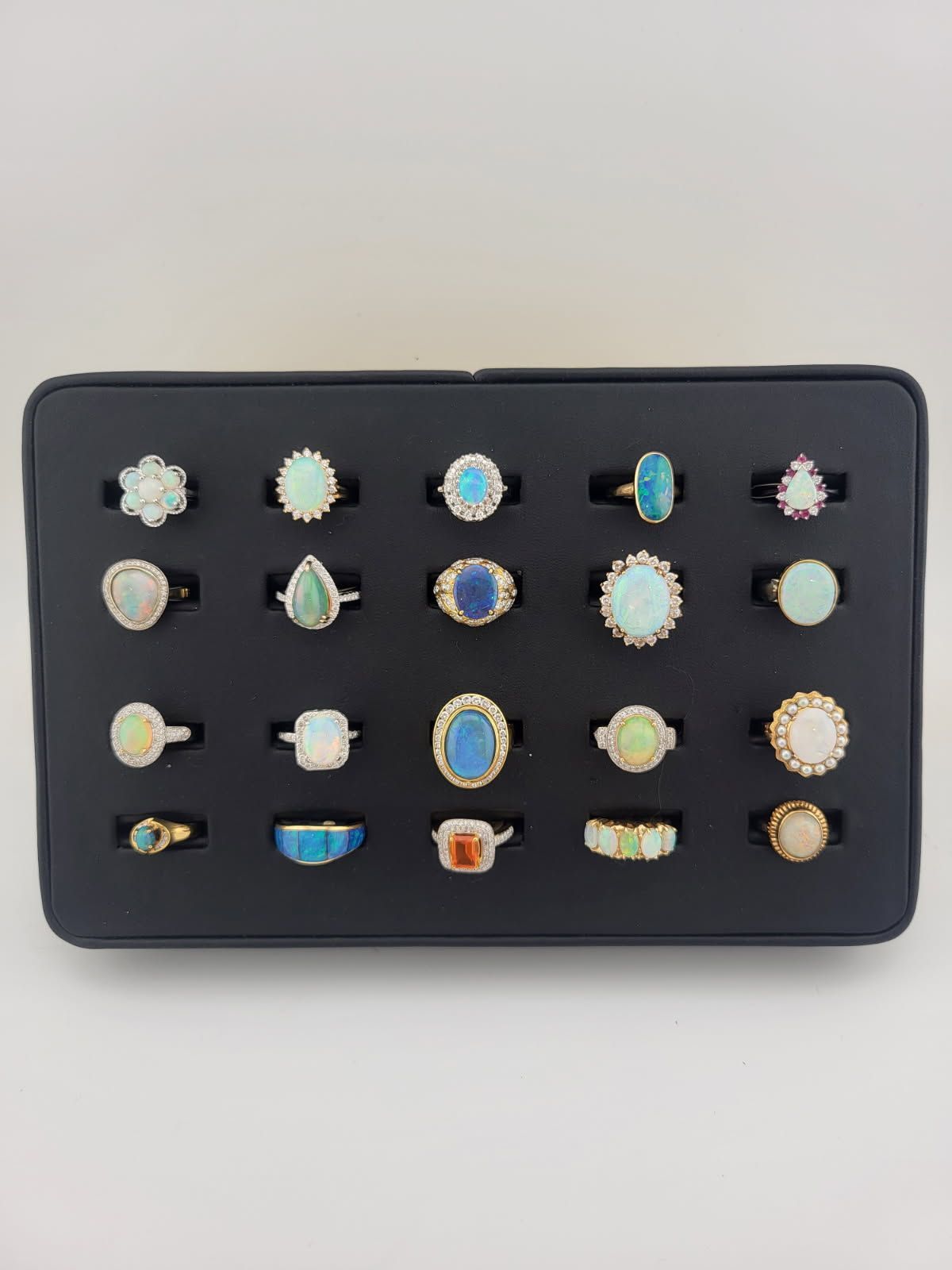 Black jewelry tray filled with opal rings of various shapes and settings.