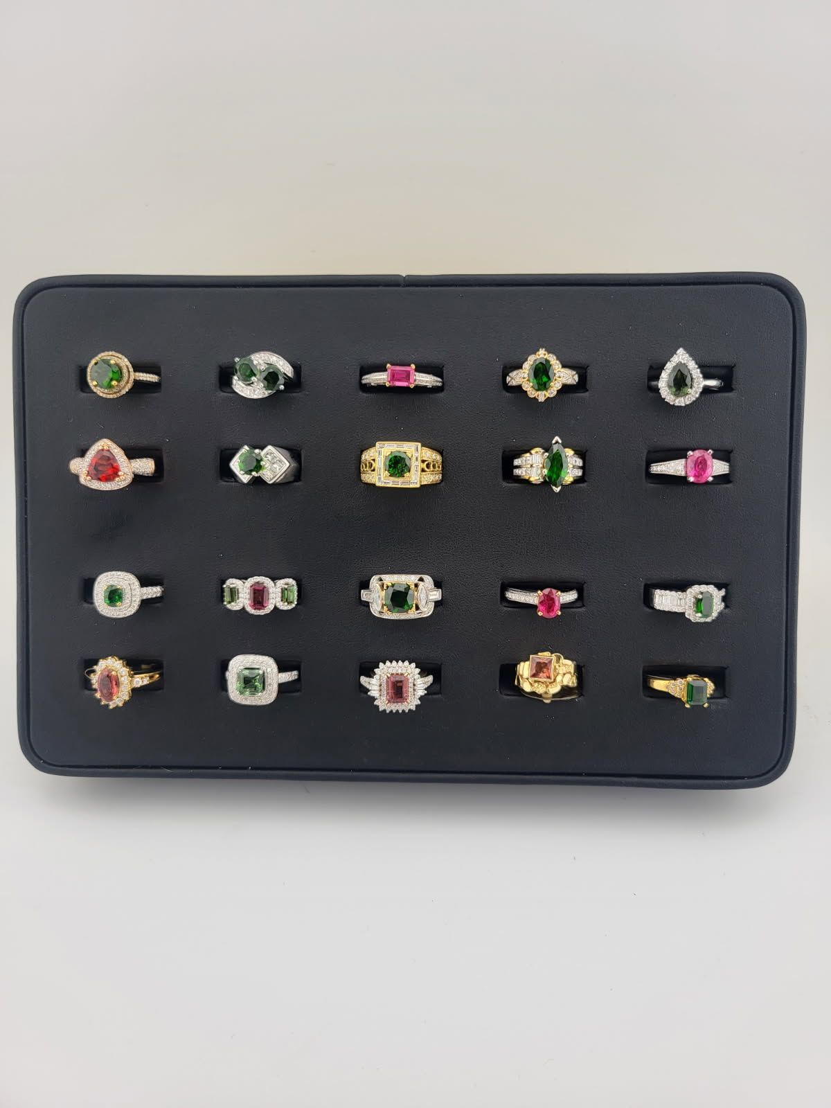 A tray of gemstone rings, with various shapes and settings in gold and silver, on a dark background.