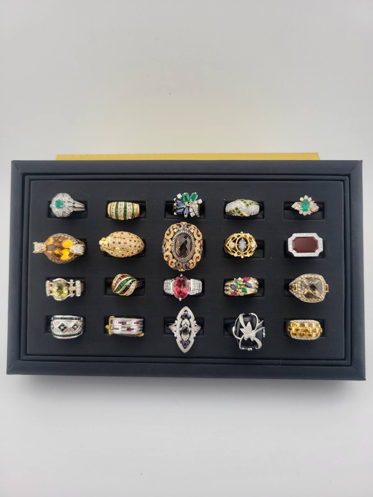Display of various ornate rings on a black tray against a white backdrop.