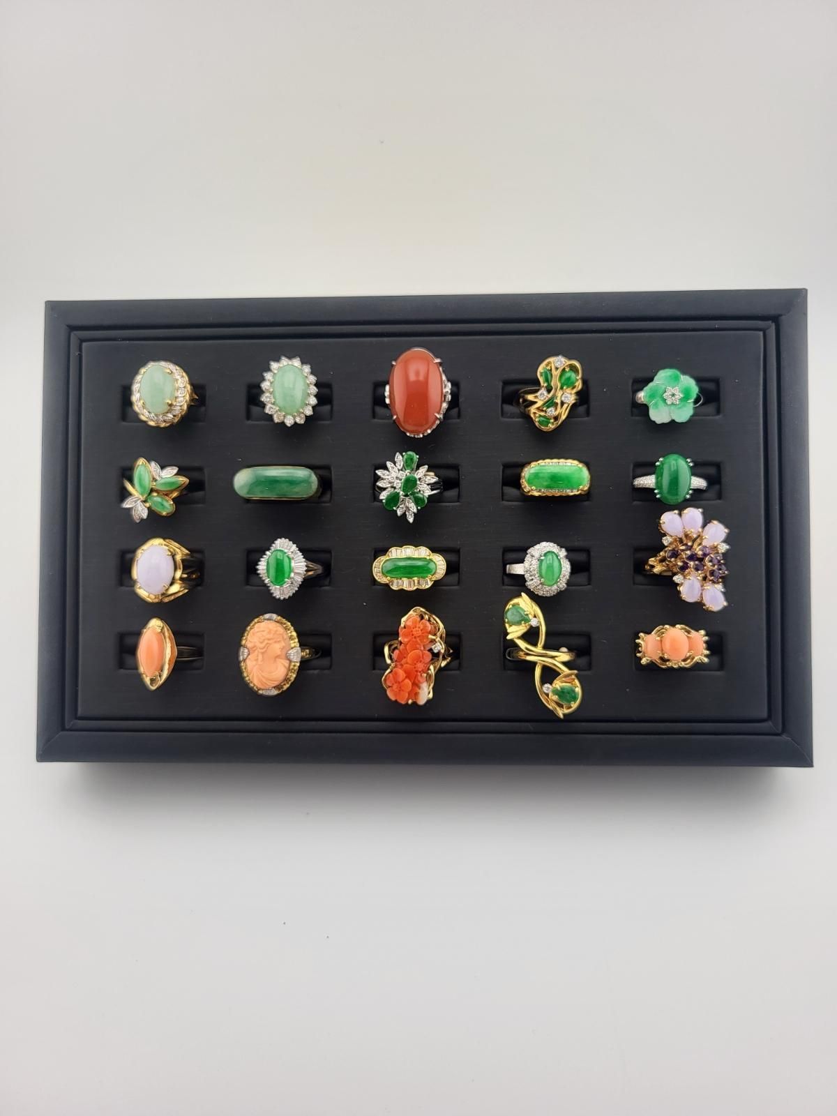 Black display tray with 24 gemstone rings in various designs and colors.