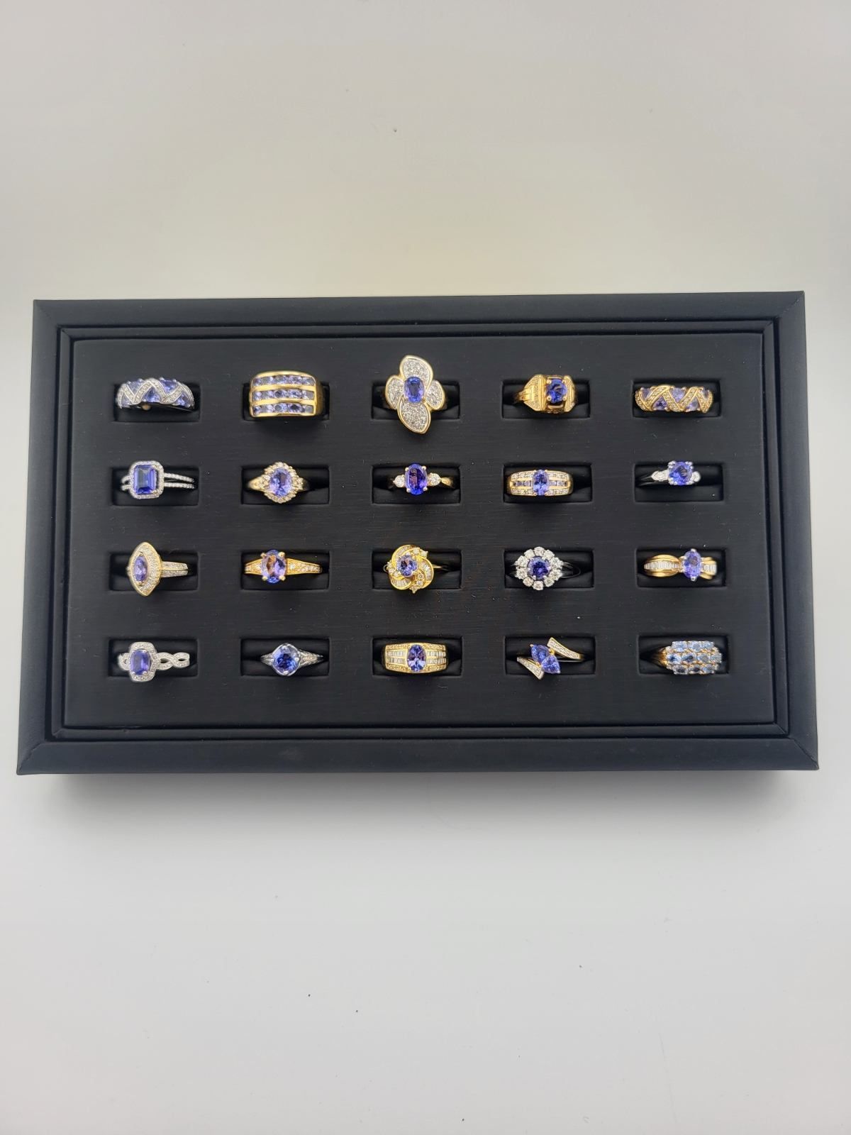 A display tray of various rings, each featuring a blue gemstone, arranged on a black surface.