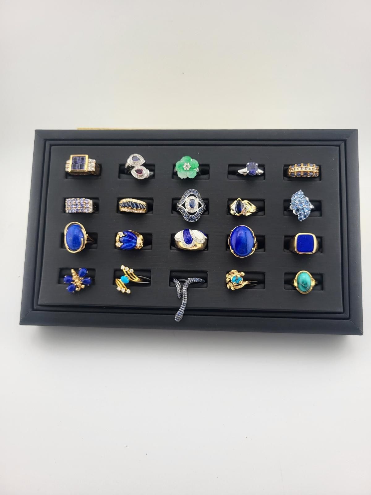 Jewelry display with twenty-four rings in a black tray against a white backdrop.