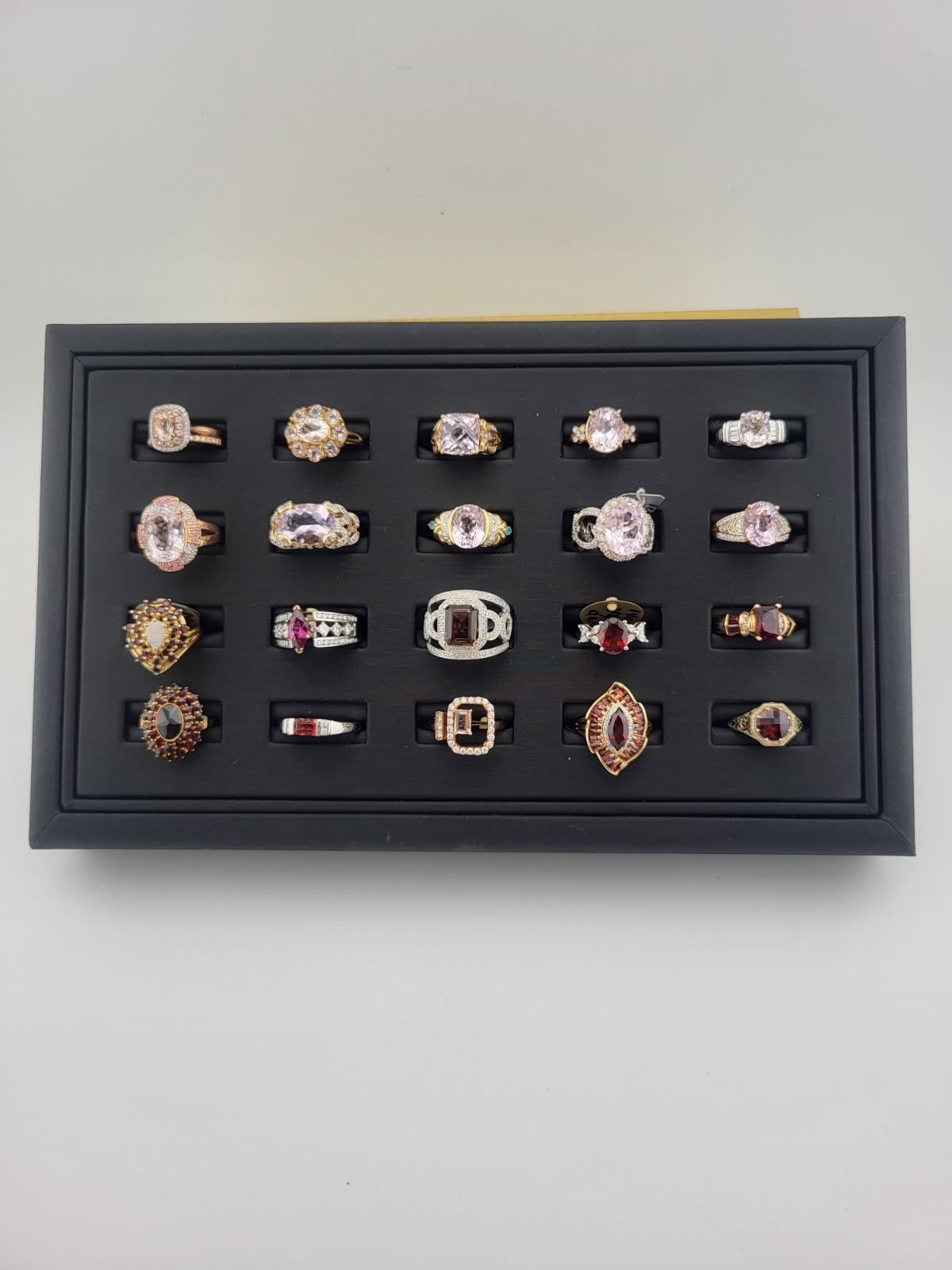Black display tray with an assortment of gemstone rings in various settings and colors.