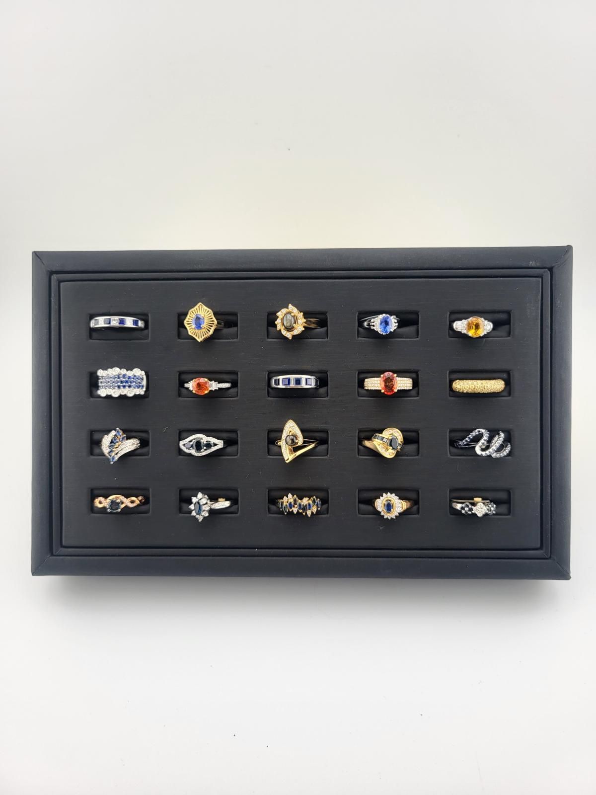 Jewelry display case with an assortment of rings. Black display with rings set in individual black slots against a white background.