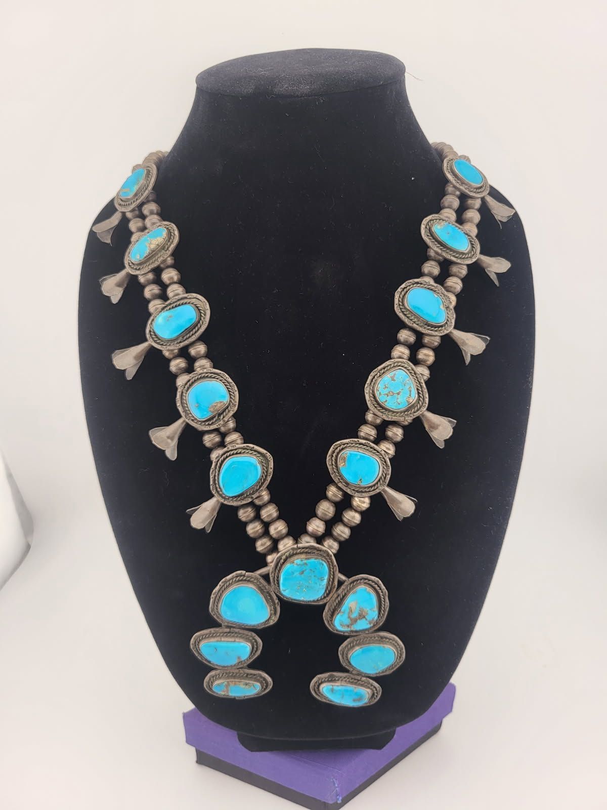 Turquoise squash blossom necklace on a black display bust. Silver and blue.