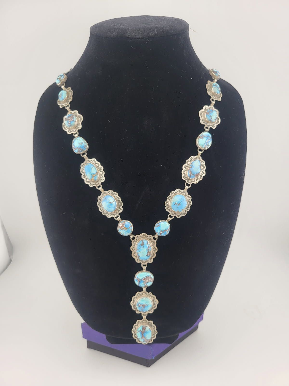 Turquoise necklace on a black velvet display stand; silver-tone filigree frames.