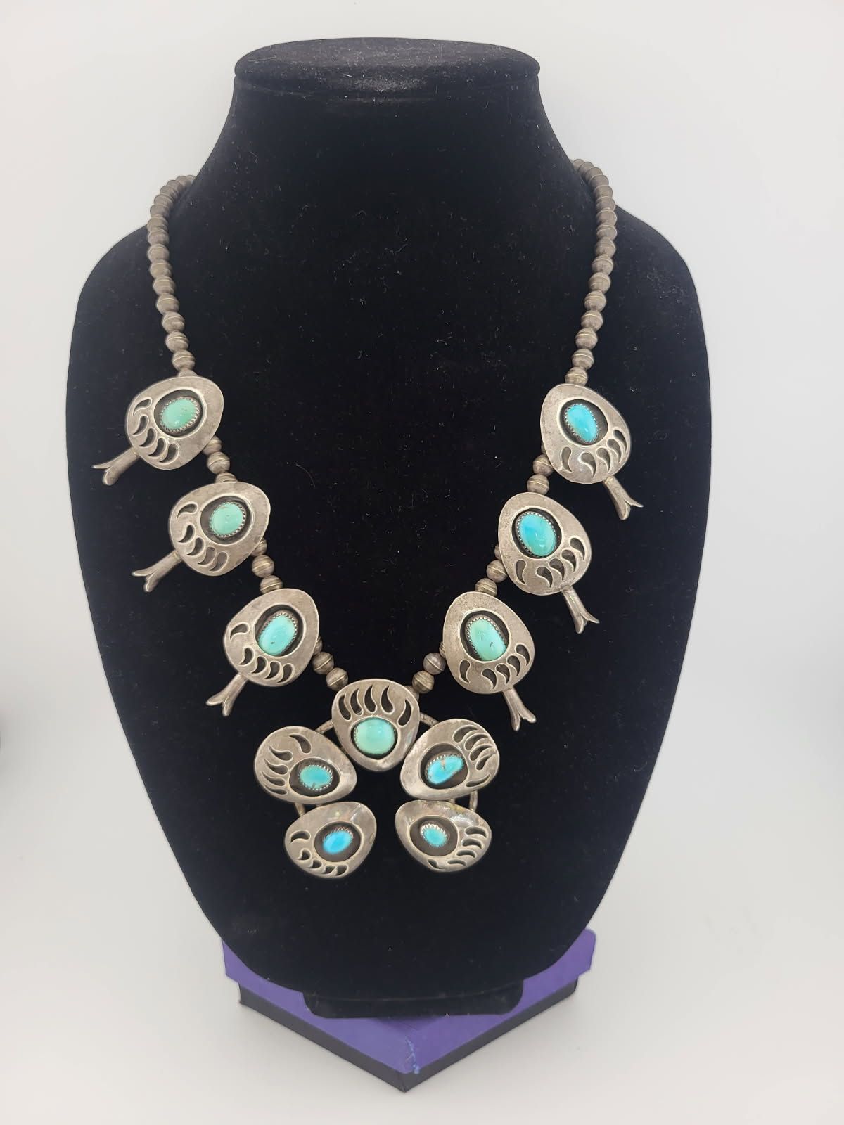 Silver turquoise squash blossom necklace on a black display stand.