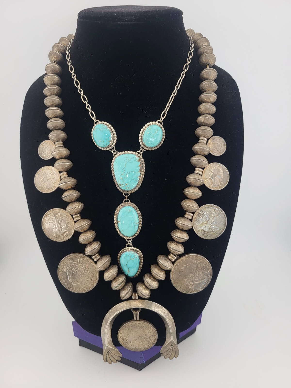 Two silver necklaces with turquoise stones on a black mannequin.