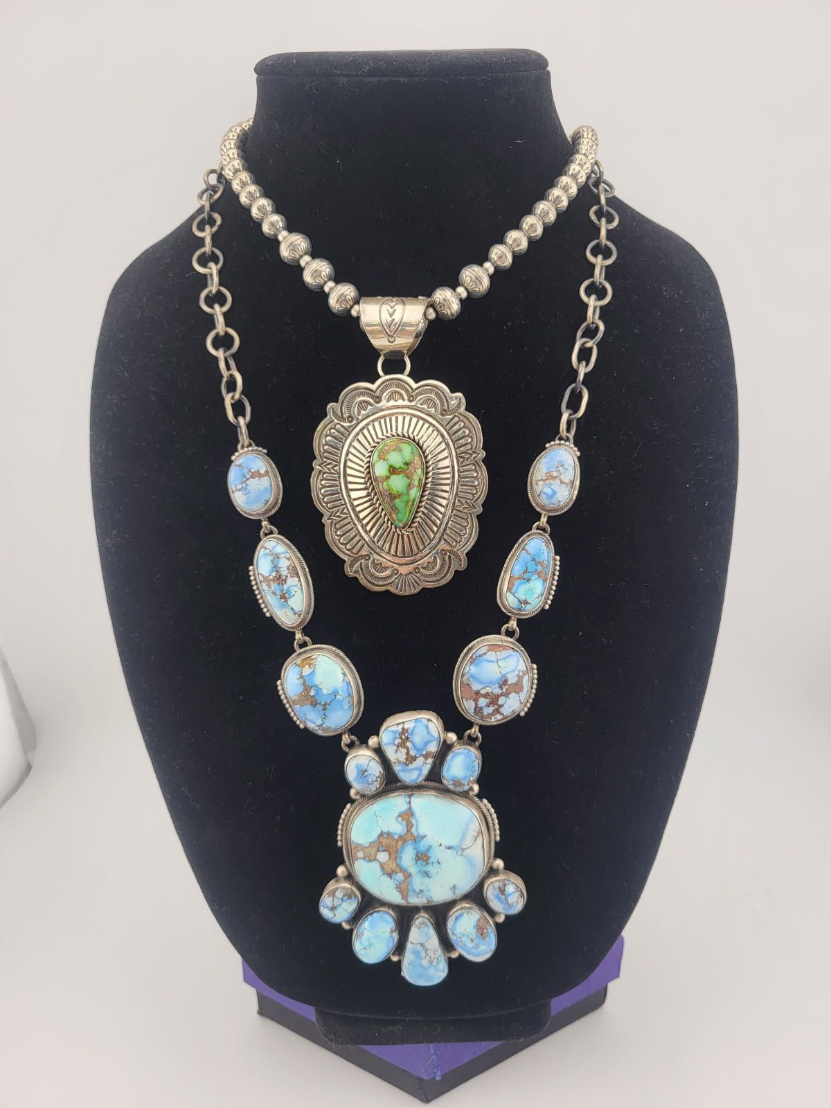 Two turquoise and silver necklaces displayed on a black jewelry bust.