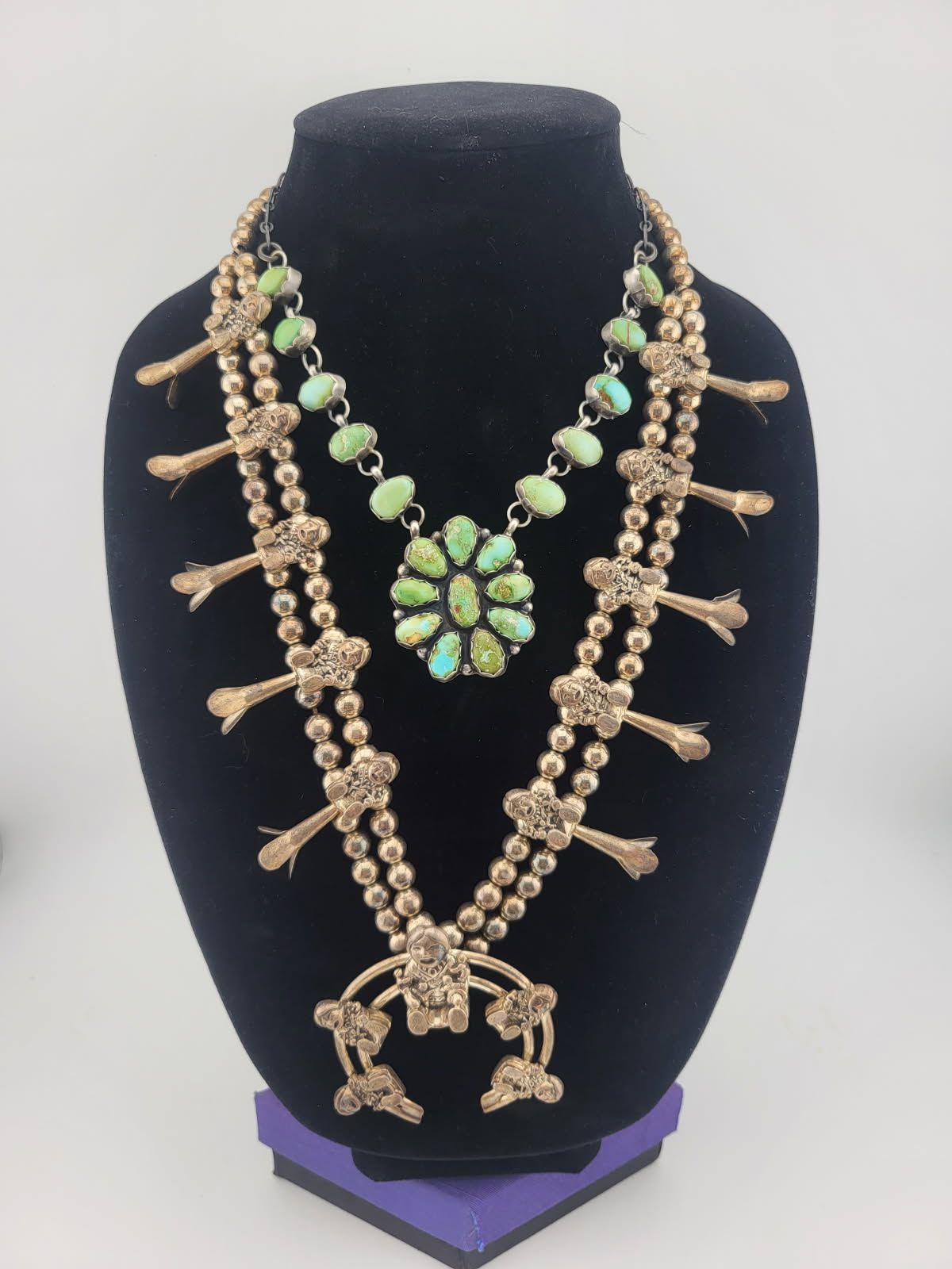 Two turquoise and silver squash blossom necklaces on a black mannequin.