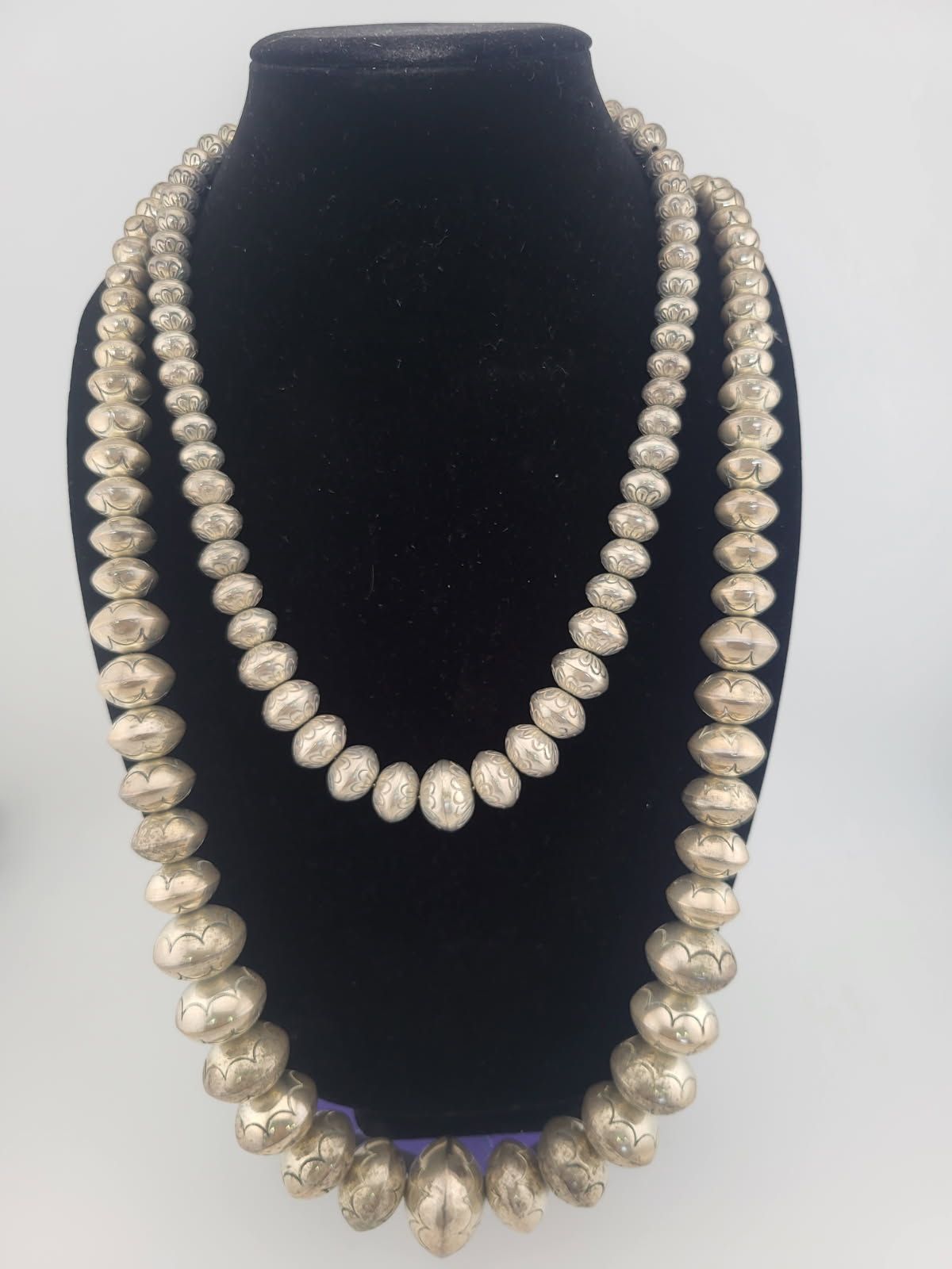 Two silver beaded necklaces displayed on a black stand.