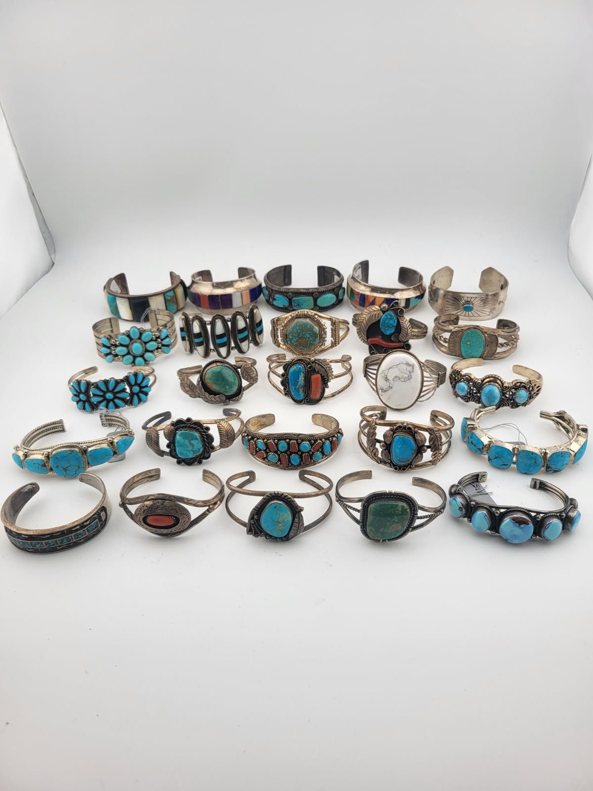 Twenty-five turquoise and silver bracelets displayed on a white surface.
