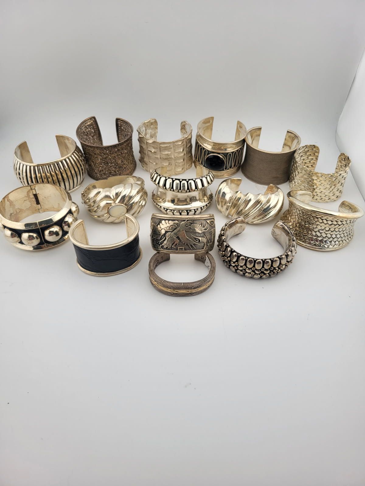 Collection of assorted gold-toned metal cuff bracelets, with various textures and designs on a white surface.