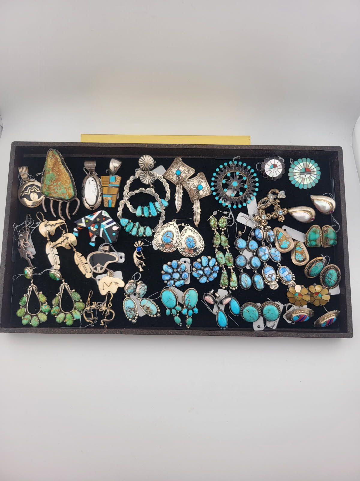 Collection of turquoise jewelry on a black velvet tray, including earrings, pendants, and rings.