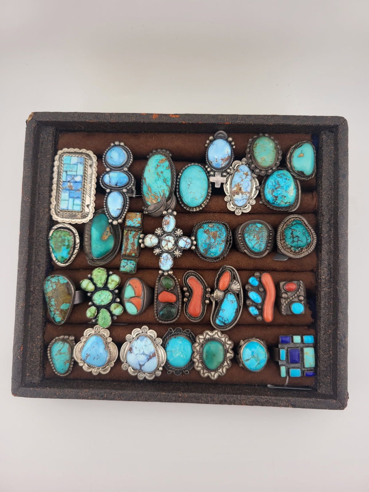 A tray filled with various turquoise and coral rings, showcasing different shapes and silver settings.