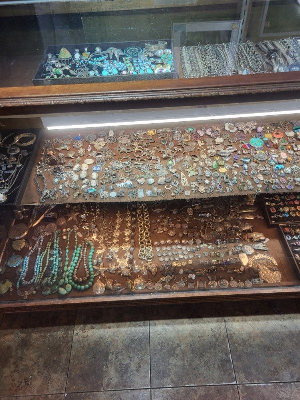 Jewelry display case with various necklaces, bracelets, and rings. Turquoise, silver, and gold items visible.