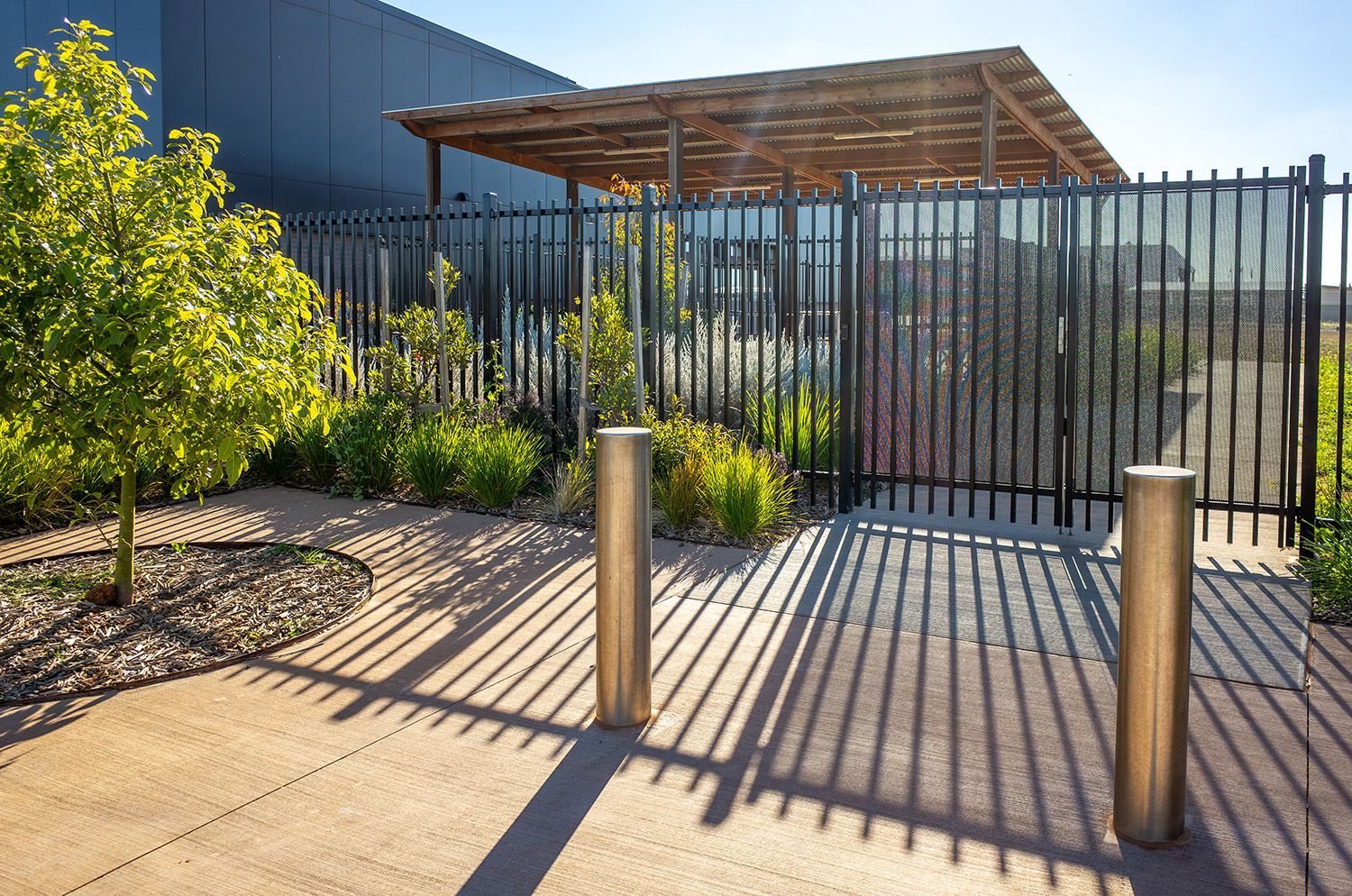 Metal security fence with bollards and landscaping at the entrance of a facility.