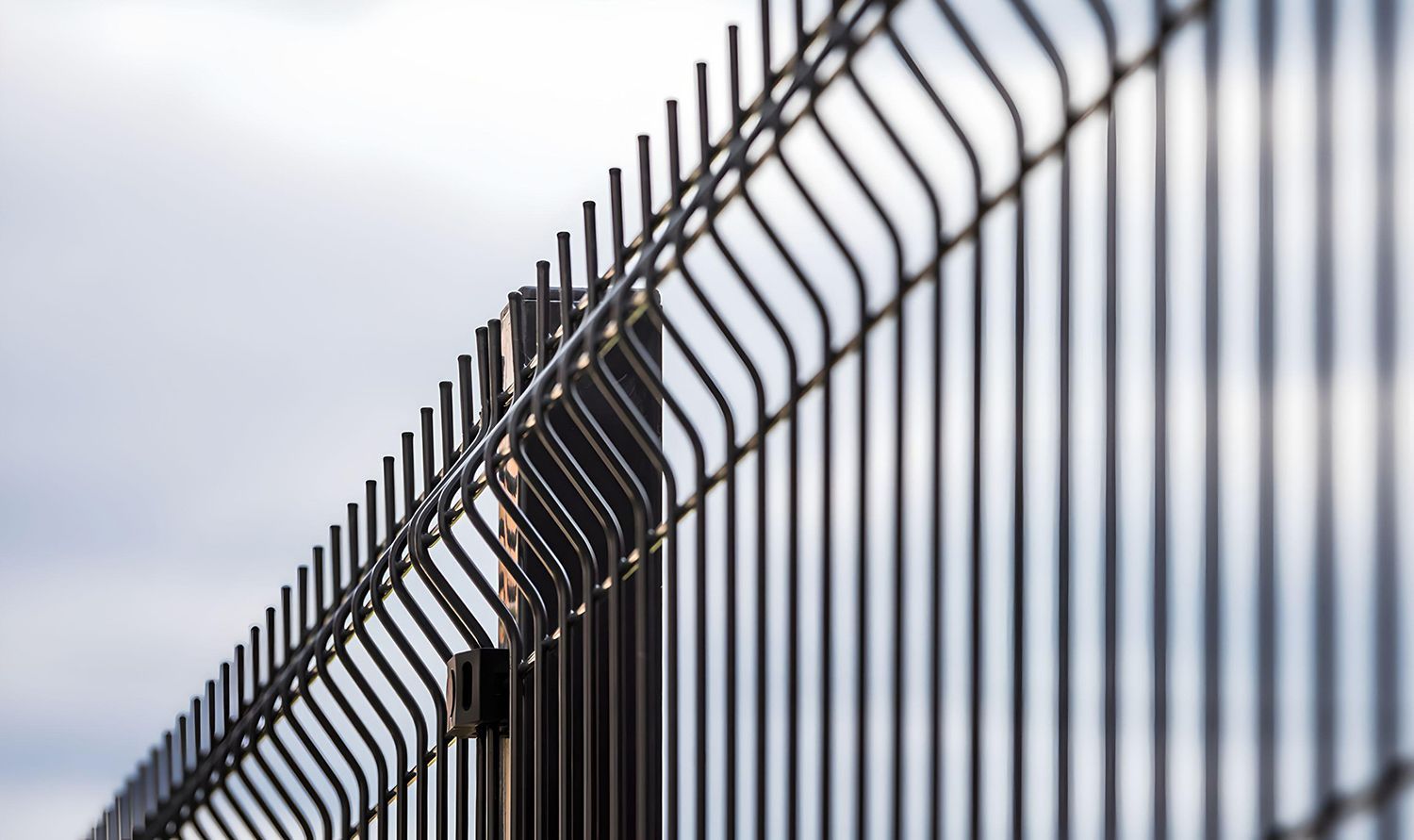 Close-up of a tall metal security fence with angled anti-climb panels. Close-up of a tall metal security fence with angled anti-climb panels.