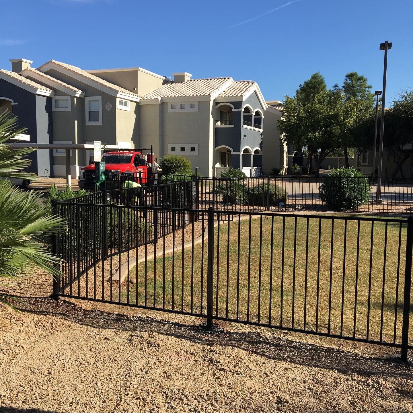 Black metal fence in front of a building. A red truck and workers are near the building in an outdoor setting.