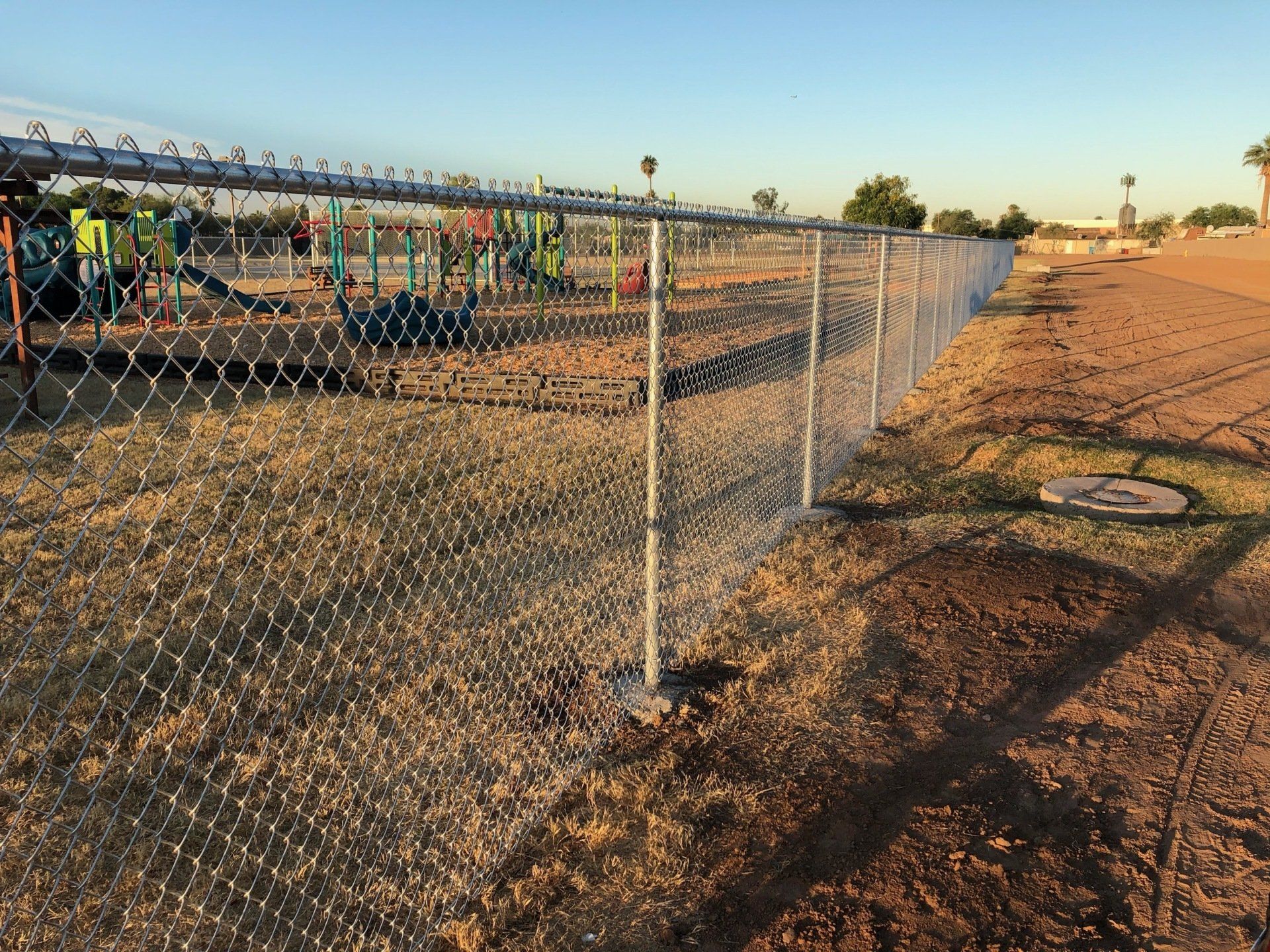 Chain-link fence surrounds a playground with colorful equipment on a sunny day.
