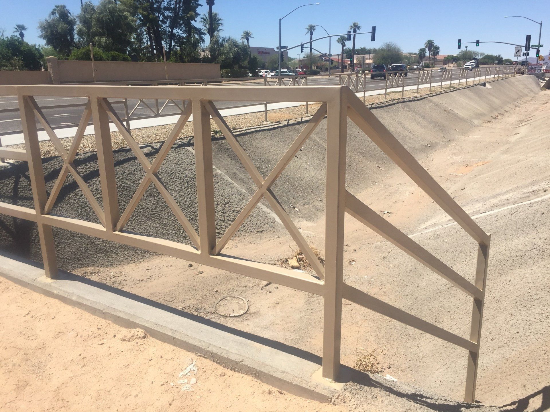 Beige metal railing alongside a dry concrete channel, road in the background.