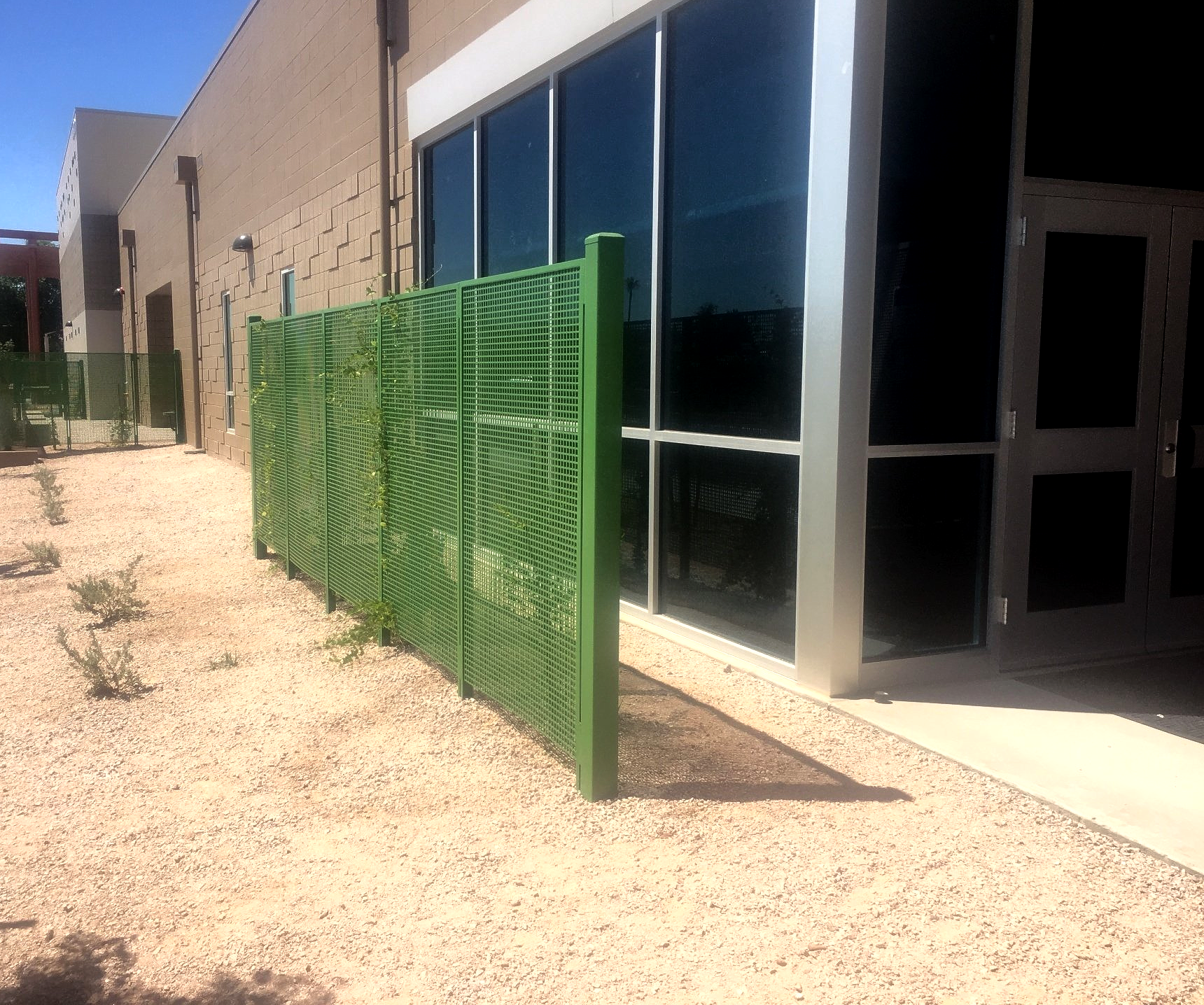 Green metal fence next to a building with large windows and a gravel area.