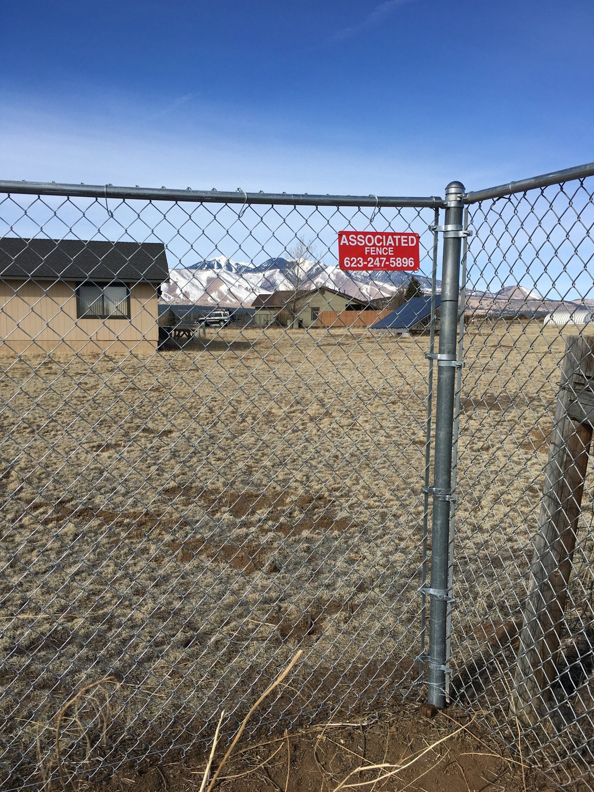 Chain link fence with a red warning sign. Houses and mountains are visible in the background under a blue sky.