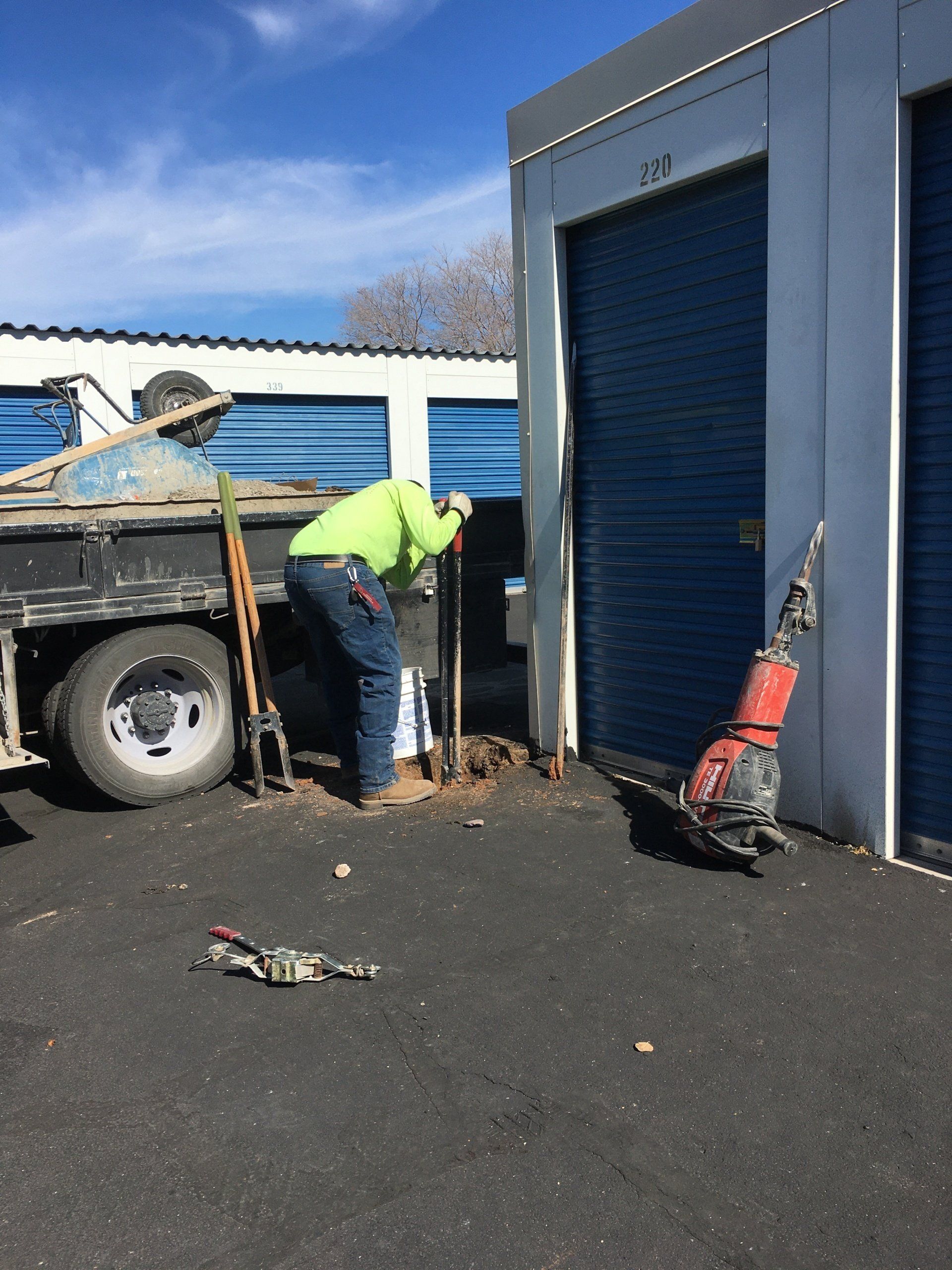 Man in neon green shirt digging near storage units.