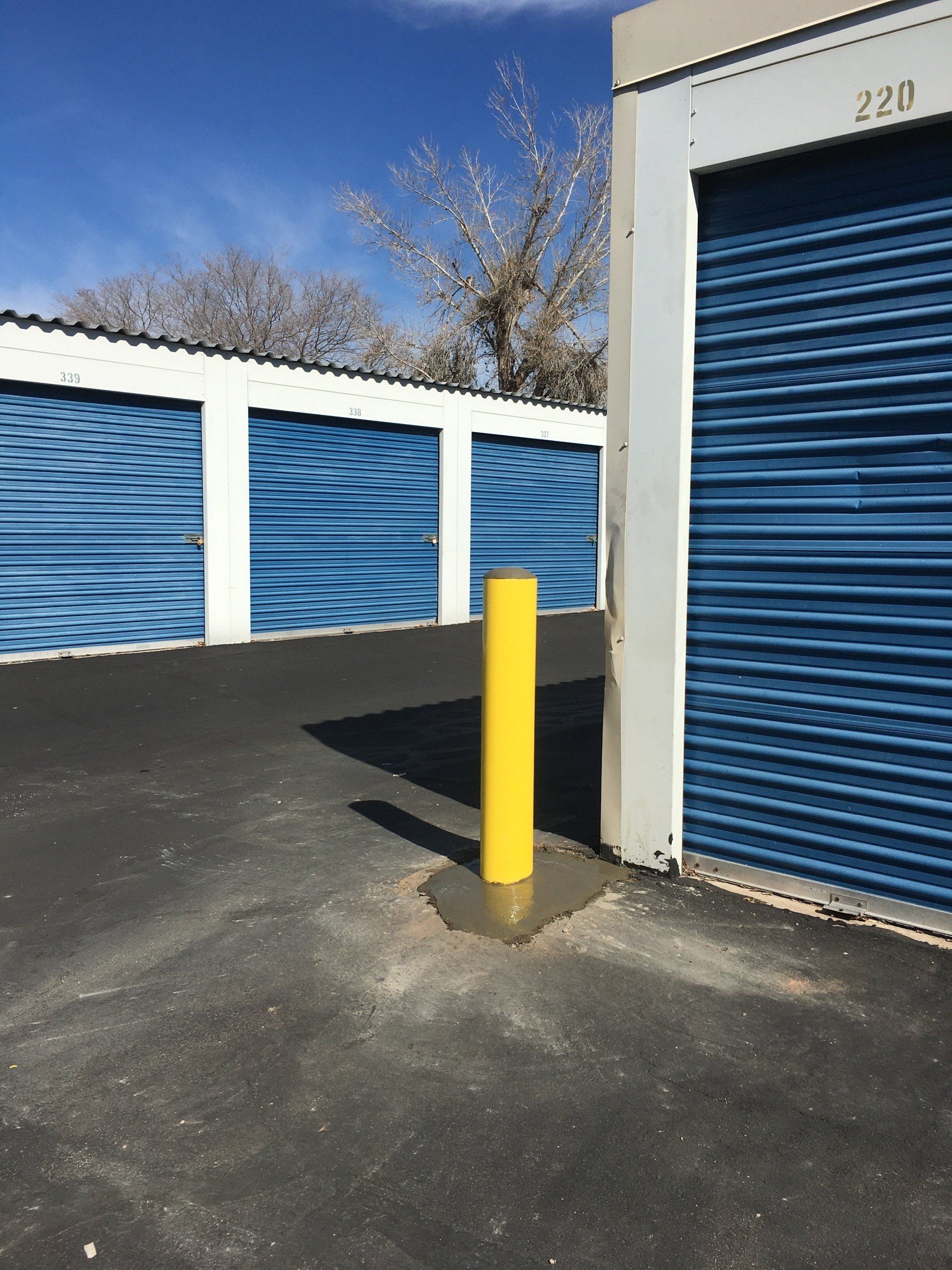 Yellow bollard in front of blue storage units on asphalt.