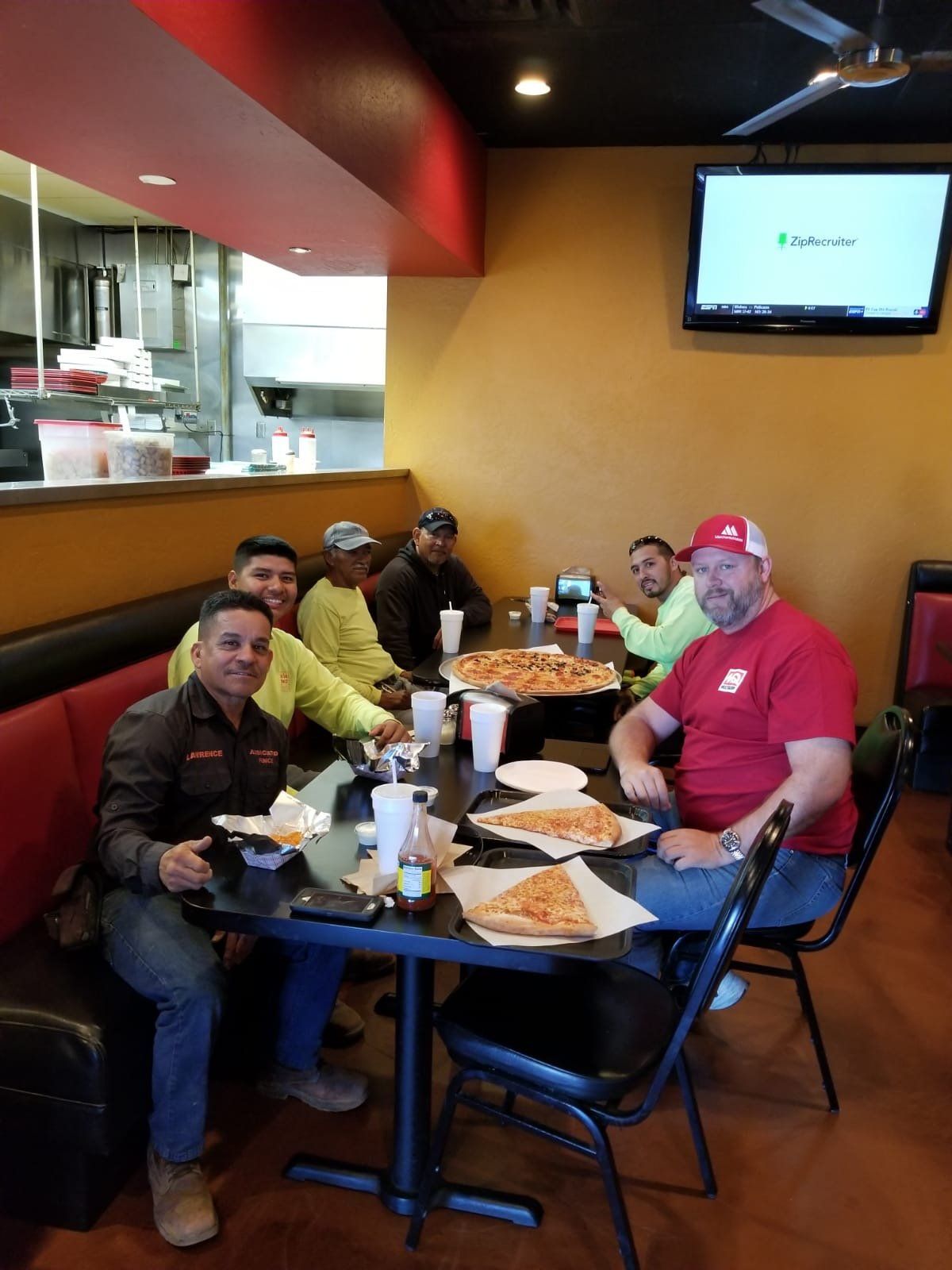 Group of men eating pizza at a restaurant; red and yellow accents.