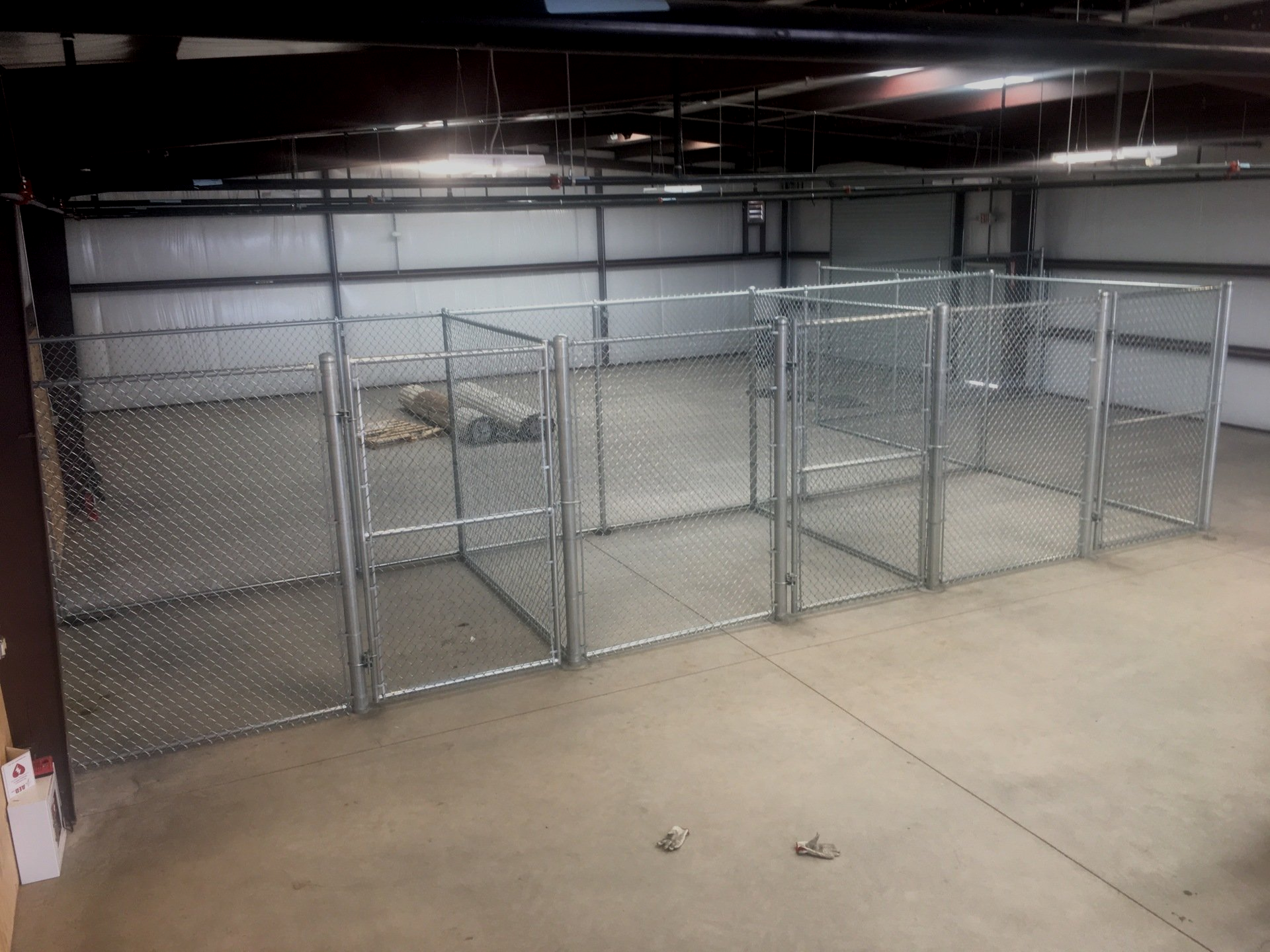 Chain-link fence enclosures inside a large industrial space. Metal supports and concrete flooring.