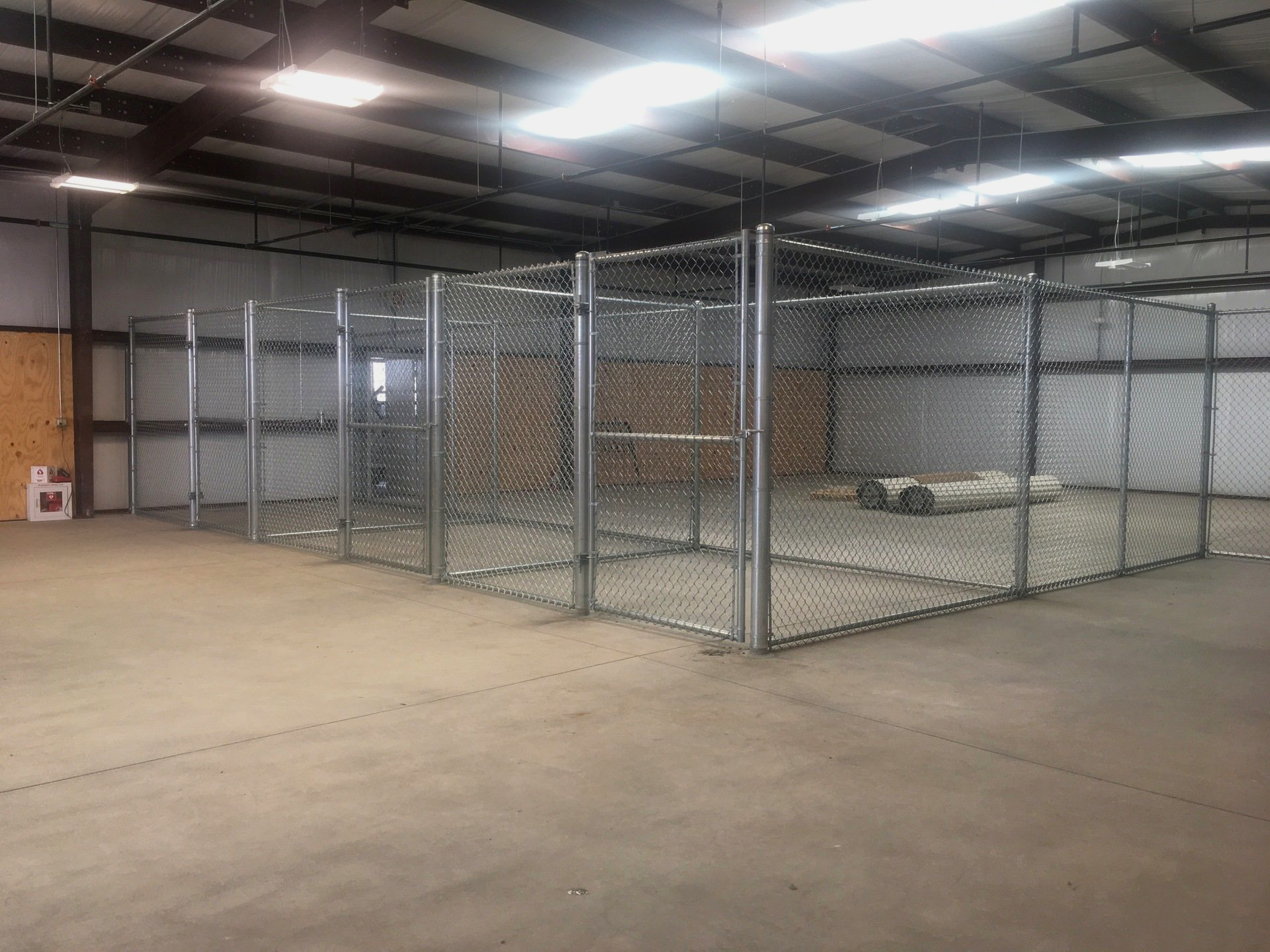 Metal chain-link storage units inside a large warehouse with a concrete floor.