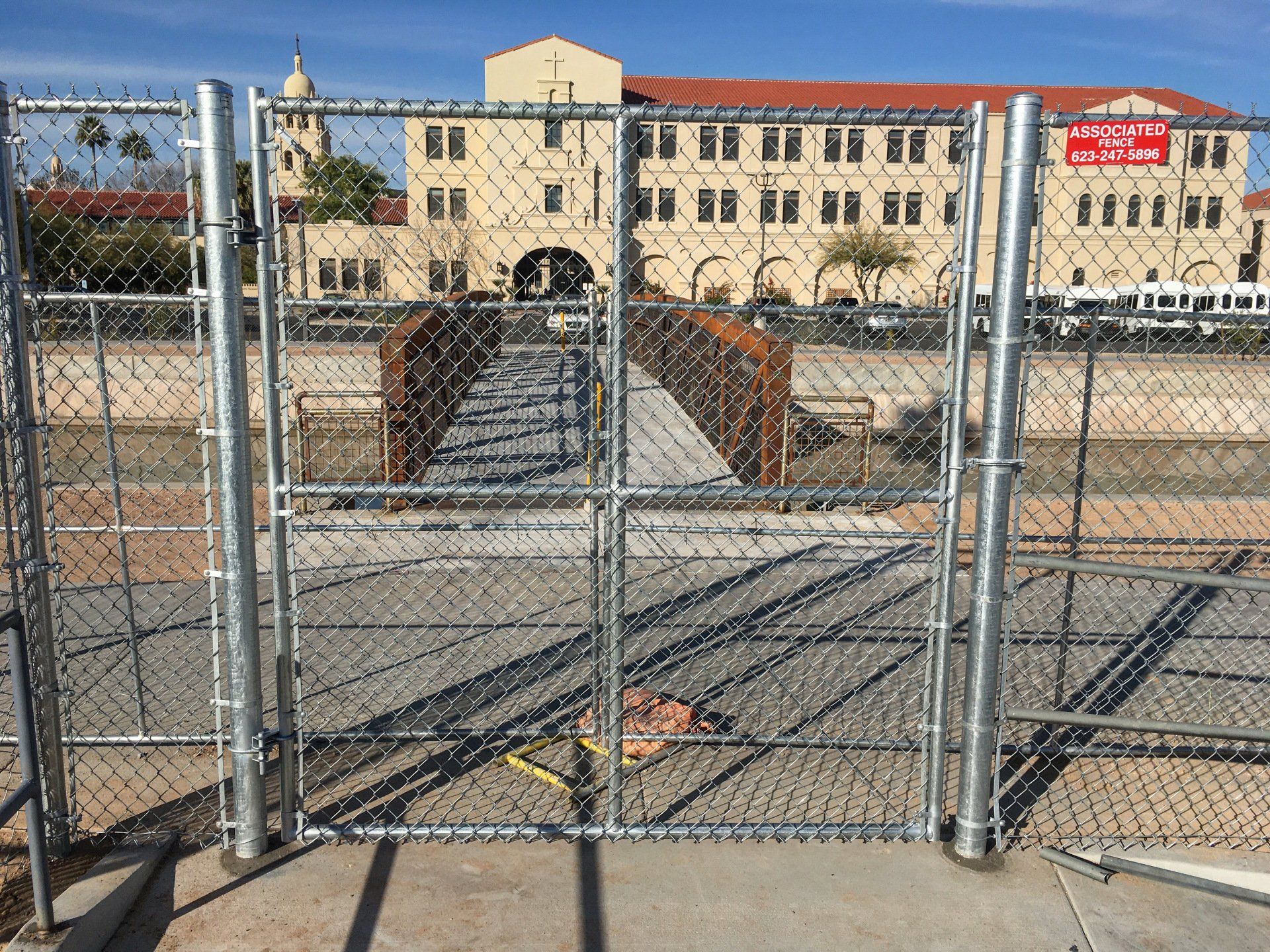 A metal chain-link fence blocks access to a bridge; a large building is in the background.